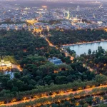 Vistas aéreas de la ciudad de Madrid durante la puesta de sol en un día despejado, pudiendo observar el Parque del Retiro, la catedral de la Almudena, el Palacio Real y el Palacio de Cristal.