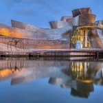 Bilbao, Spanje - 10 juli 2021: Het beroemde Guggenheim Museum weerspiegeld in de rivier de Nervion bij zonsopgang