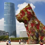Bilbao, Spanje - 30 augustus 2013: Toeristen fotograferen de grote gebloemde hond 'Puppy', die is ingekaderd als het kussen van een gebouw; de Iberdrola wolkenkrabber