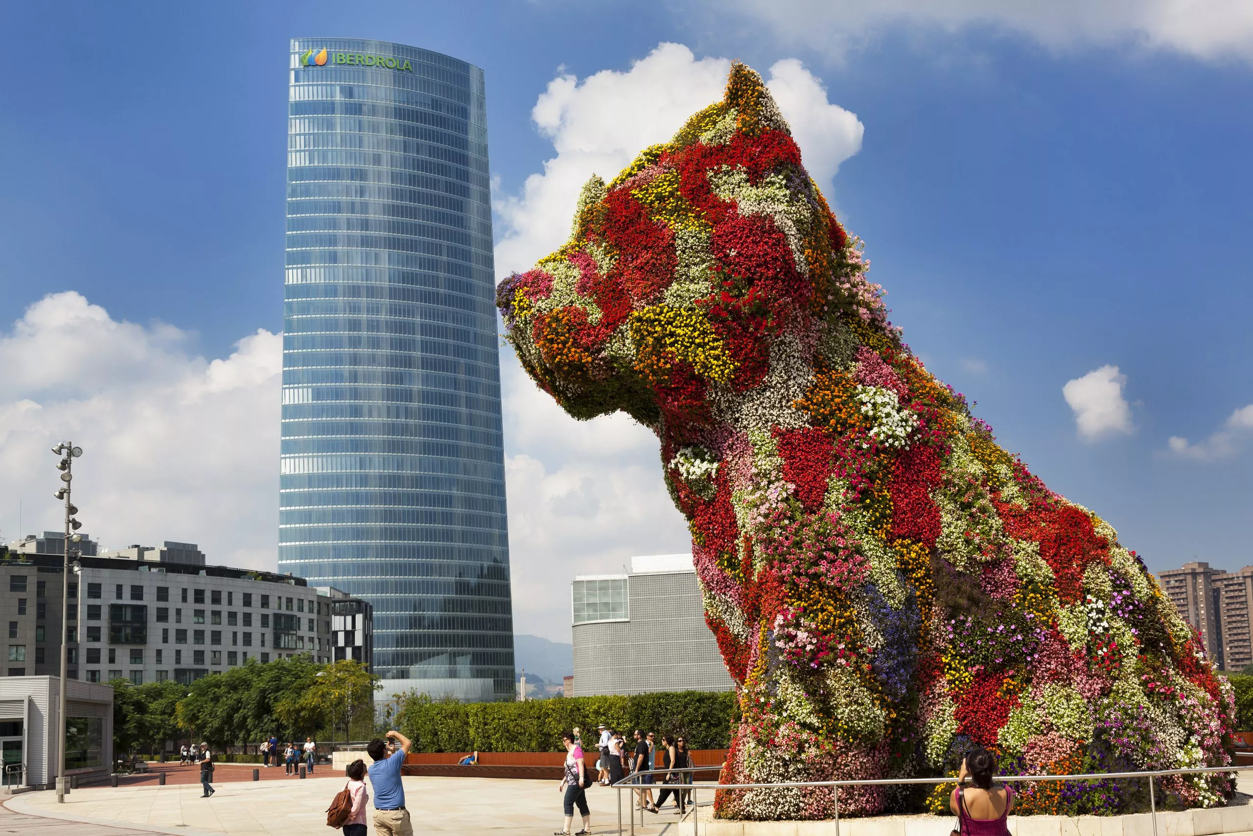 Bilbao, Spain - August 30, 2013: Tourists photographing the big floral dog 'Puppy', that is framed as kissing a building; the Iberdrola skyscraper