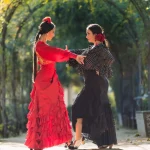 Verticale foto van twee vrouwen in flamencojurken die samen dansen in een tuin met een plantenboog