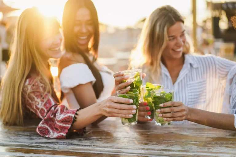 Multiracial girls having fun cheering with cocktails at bar on the beach - Focus on front hands holding drinks