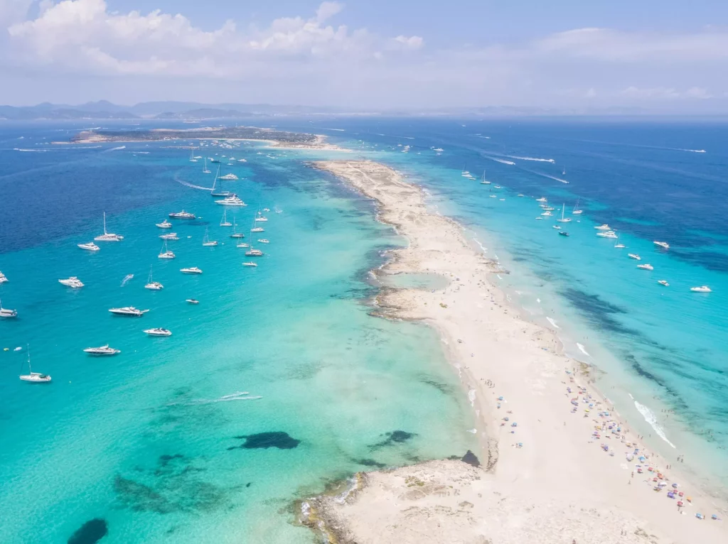 Luftfoto af en stor mængde lystbåde, der ligger for anker ud for Formentera Ibizas kyst, med turkisblåt Middelhav og havblåt vand.