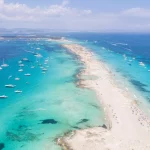Luftfoto af en stor mængde lystbåde, der ligger for anker ud for Formentera Ibizas kyst, med turkisblåt Middelhav og havblåt vand.