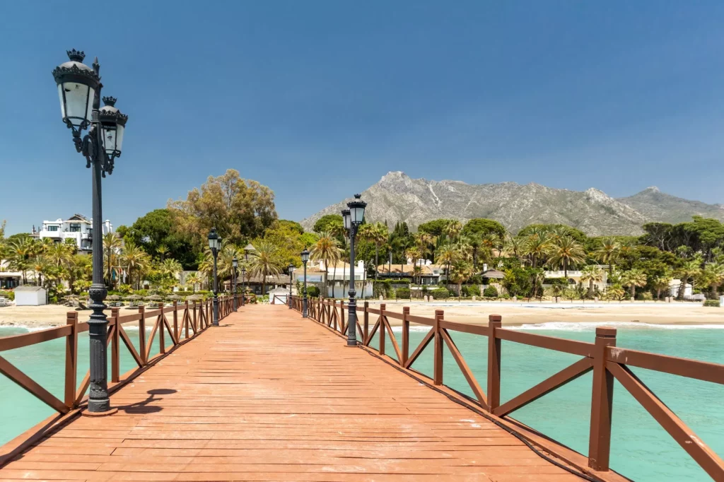 Uitzicht op rode houten brug "Embarcadero" in Marbella. Uitzicht op luxueuze wijk Puente Romano, dure urbanisaties. Berg "La Concha". Spectaculaire reisbestemming. Smaragdgroen water, geen mensen