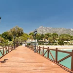 Uitzicht op rode houten brug "Embarcadero" in Marbella. Uitzicht op luxueuze wijk Puente Romano, dure urbanisaties. Berg "La Concha". Spectaculaire reisbestemming. Smaragdgroen water, geen mensen