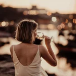 una dama en traje de noche con un vaso de vino blanco disfrutando de la puesta de sol sentada a orillas del río Duero.
