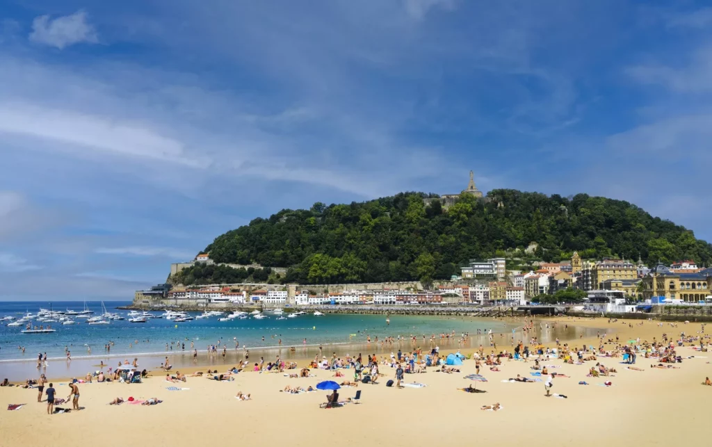 Landscape of La Concha beach in the city of San Sebastian, in the Spanish Basque Country, on a sunny day with people enjoying the beach and Mount Urgull in the background.