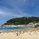 Landscape of La Concha beach in the city of San Sebastian, in the Spanish Basque Country, on a sunny day with people enjoying the beach and Mount Urgull in the background.
